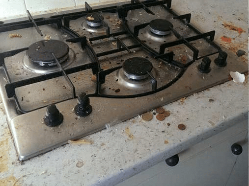 Table de cuisson à gaz en inox sale avec débris alimentaires, miettes et pièces de monnaie sur le plan de travail.