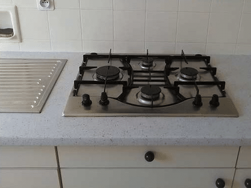 Plaque de cuisson à gaz inox 4 feux encastrée sur plan de travail gris clair avec crédence carrelée blanche.