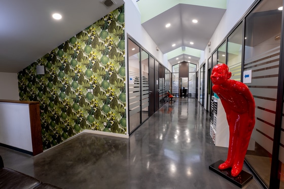 Design de Bureau Moderne : Couloir avec Statue et Mur Végétal Bureau moderne au design créatif avec mur végétal, sculpture rouge et couloir lumineux en béton ciré.