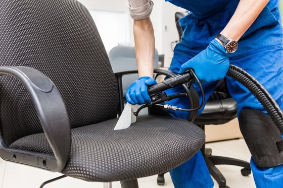 Nettoyage de chaise de bureau par un professionnel Professionnel en tenue bleue nettoyant une chaise de bureau noire avec une machine à injection-extraction.