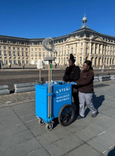 Service de nettoyage STANI Place de la Bourse Bordeaux Deux agentes poussent un chariot de nettoyage STANI devant la Place de la Bourse à Bordeaux sous un ciel bleu.